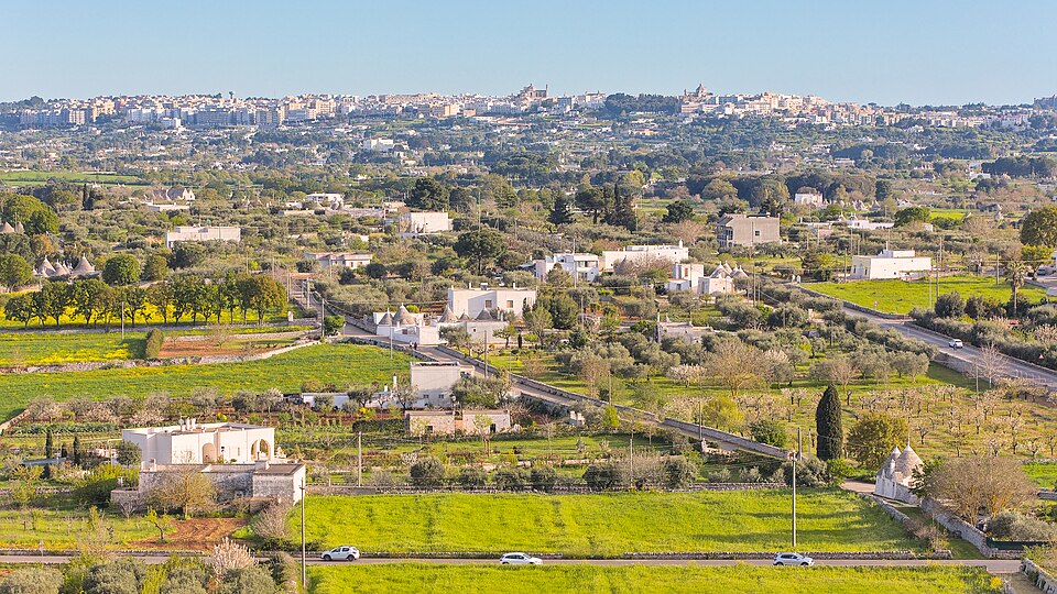 Vista desde Via Nardelli hacia campos, olivos y trulli del Valle d’Itria, con Martina Franca en el horizonte